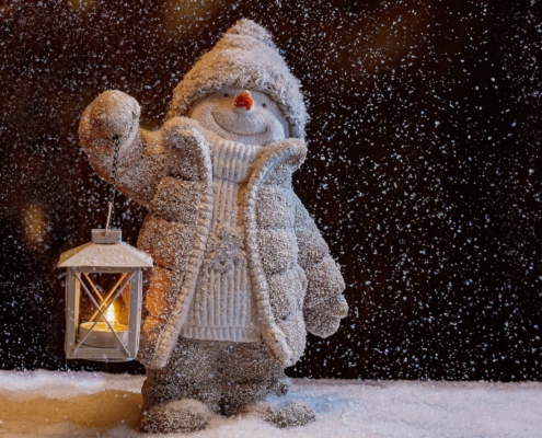 Winter image of a snowman holding a lantern a snowy night.