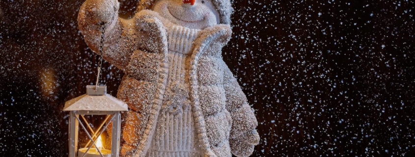 Winter image of a snowman holding a lantern a snowy night.